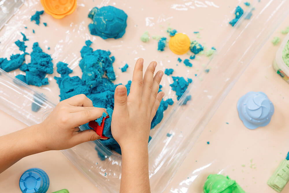 child playing with blue magic sand and colorful toys