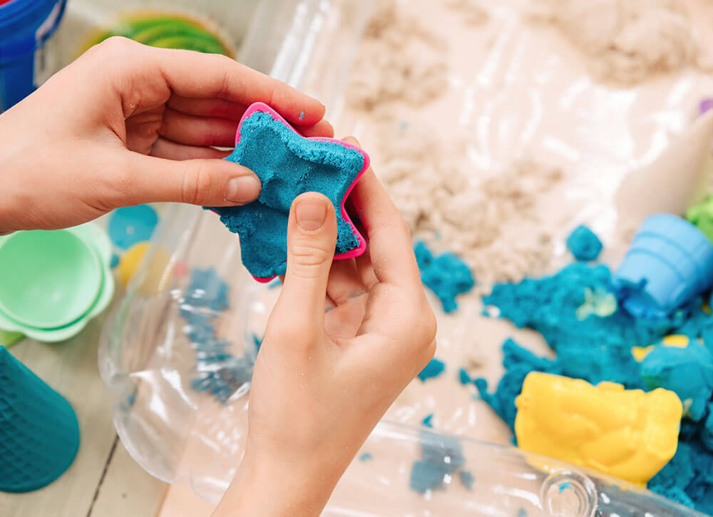 child hands holding blue star magic sand mold near colorful toys