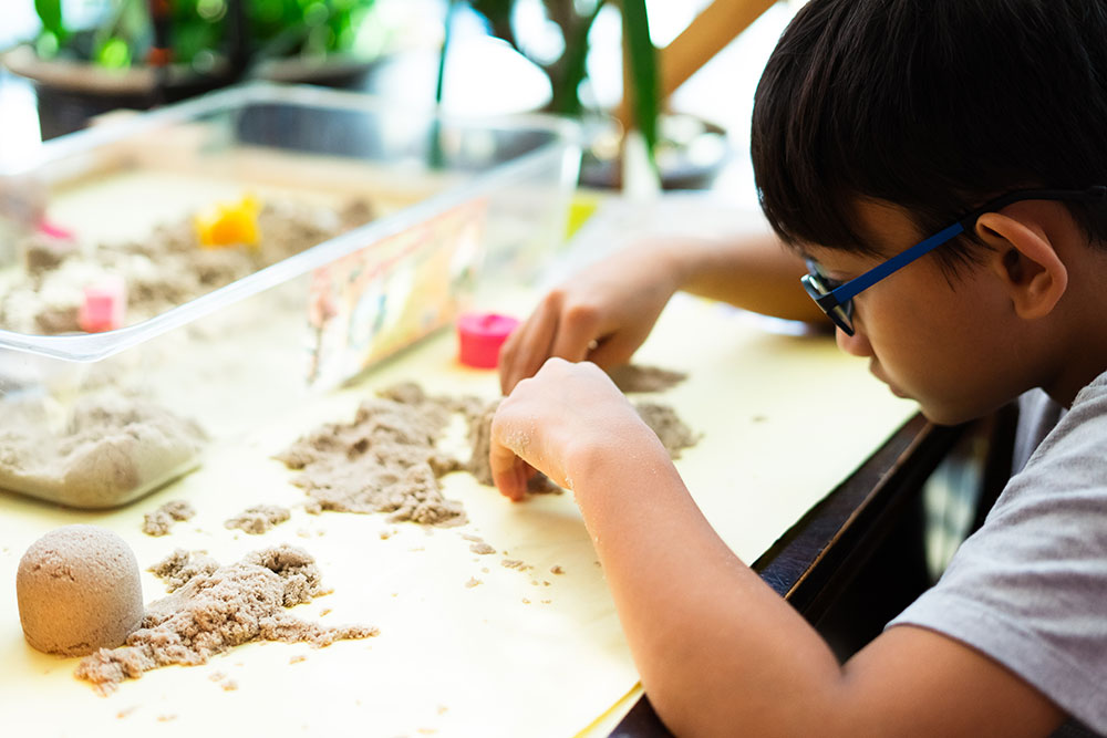 child playing with kinetic sand at table