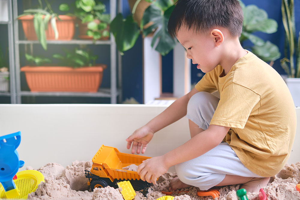 Child playing with toy trucks in a sandbox of Magic Sand