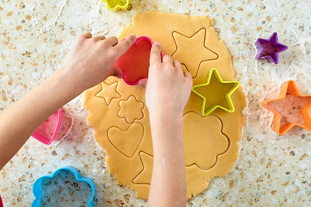 Child shaping kinetic sand with colorful cookie cutters