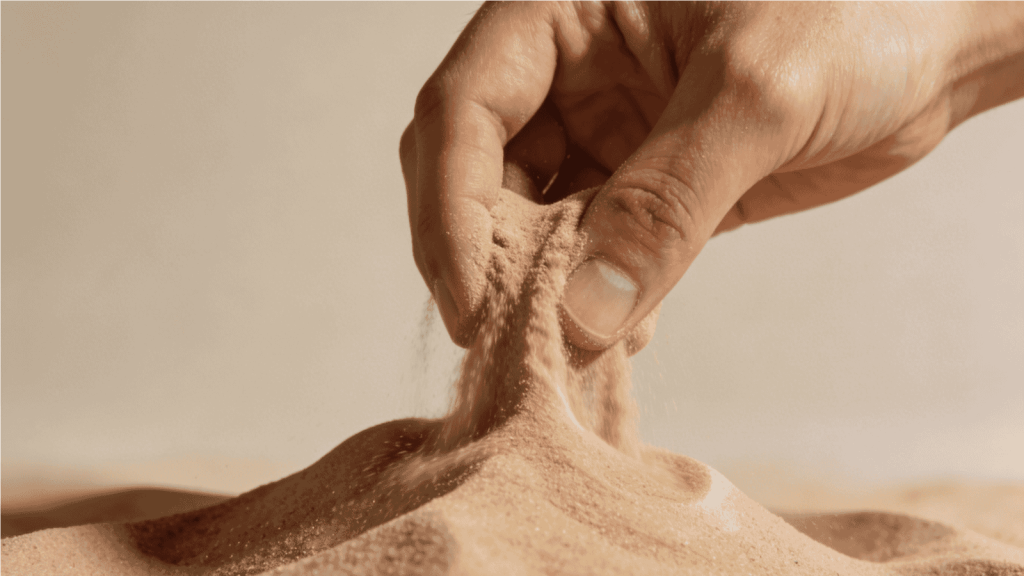 hand pouring kinetic sand onto a mound